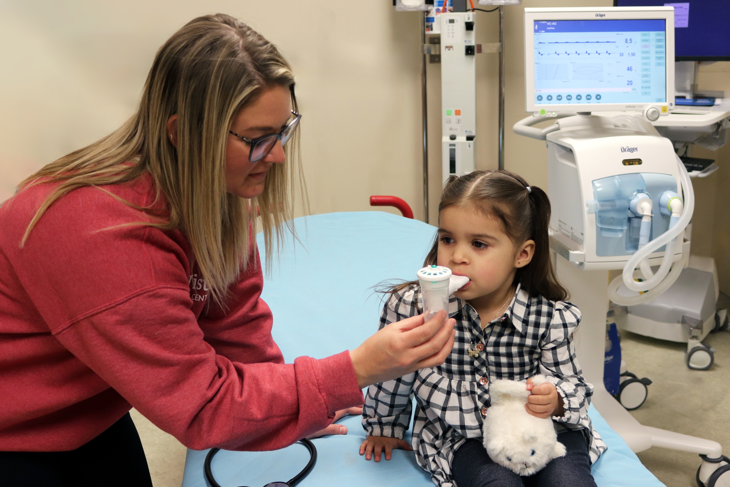 BVMRC Respiratory Therapist uses a breathing exercise tool on a pediatric patient in the Emergency Room at BVRMC, the pediatric ventilator is shown behind them