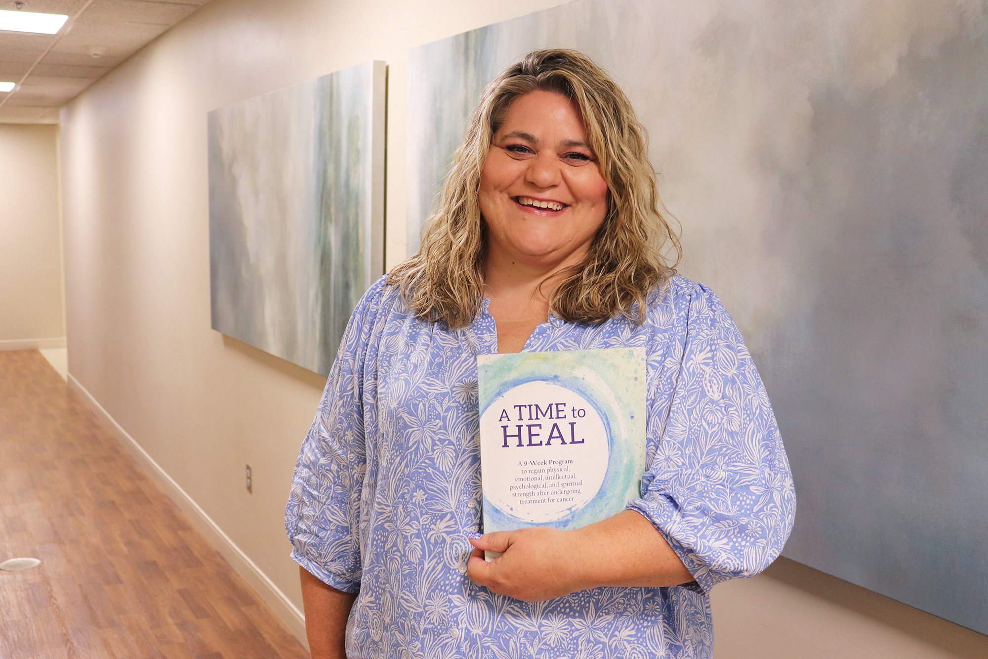 BVRMC Social Worker holding a book titled, "A Time to Heal" in a hallway at BVRMC.